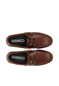 Brūni ādas apavi ar noapaļotu degunu, dekoratīvo šuvēm un zelta acīm. Iekšdaļa ir tumša, ar "BIANCO" balta drukāta.