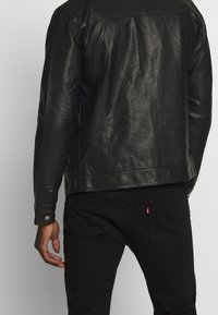 Veste en cuir noir au toucher lisse, présentant un design classique, des boutons-pression et une silhouette légèrement cintrée.