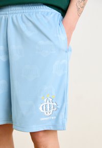 Helle blaue Sportshorts mit einem subtilen Muster aus Herzen und Klavieren, mit gesticktem Logo und drei gelben Sternen. Mit elastischem Bund.