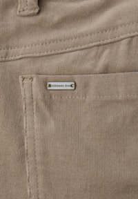 Beige korduroy-kangas, jossa on hienoja uria, ja siinä on pieni hopeinen tagi, jossa lukee "Street One." Saumadetailit näkyvät taskussa.
