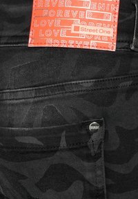 Svarta jeans med camouflagemönster i denim, med en orange "Street One" -etikett och en metallnitar på bakfickan som säger "DENIMLOVE."