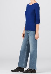 Haut en maille bleu à manches longues, assorti à un jean large bleu clair avec un ourlet effiloché. Bottines noires complètent la tenue.