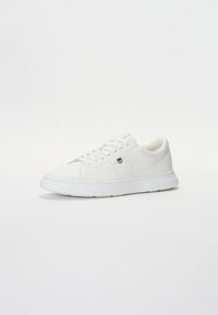 Sneakers bianchi in pelle con texture liscia, punta tonda, suola piatta in gomma bianca e design minimalista. Presentano dettagli del logo sottili.