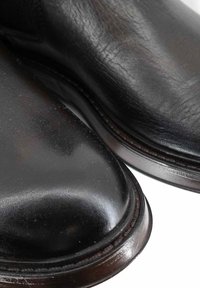 Scarpe in pelle nera con finitura lucida, punta arrotondata, dettagli testurizzati a contrasto e cuciture lungo la suola.