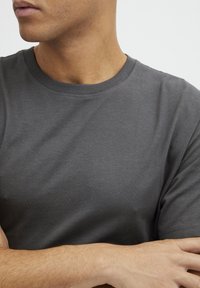 Camiseta de algodón gris con cuello redondo, mangas cortas y una textura suave. Presenta un diseño simple sin patrones ni acentos.