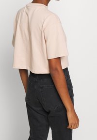 Kortärmad t-shirt med avskuren design i mjuk ljusrosa bomullstyg. Har en rund halsringning och en avslappnad passform. Bärs med högmidjade svarta jeans.