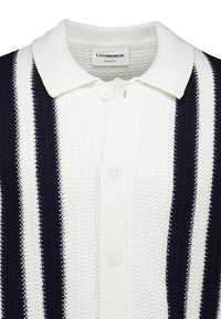 Polo blanc en maille avec des rayures verticales noires et blanches, patte de boutonnage, et col plié portant l'étiquette "Lindbergh Relaxed Fit".