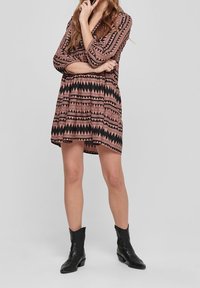 Black and pink patterned dress with geometric designs, three-quarter sleeves, and a flared shape, paired with black ankle boots.