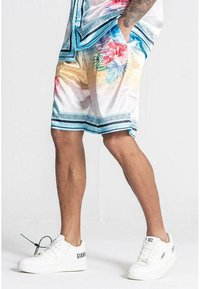 Blomster-mønstrede shorts i pastelfarver med blå detaljer, der har sidelommer og en let, glat tekstur, parret med hvide sneakers.