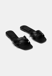 Schwarze Rutsch-Sandalen mit überkreuzten Riemen, einer flachen Sohle und einem quadratischen Zehendesign. Hergestellt aus glattem Material mit minimalistischem Design.