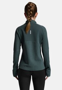 M�ørk teal pullover med en struktureret overflade, høj krave og lange ærmer. Har et hvidt vertikalt akcent på ryggen.