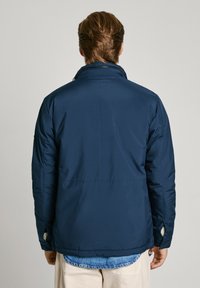 Marinblå isolerad jacka med hög krage, dragkedja fram och elastiska ärmslut. Tyget ser slätt ut med minimal synlig sömnad.