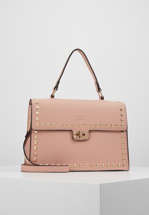 Sac à main en cuir rose blush avec garniture cloutée dorée, poignée supérieure, fermeture avant et bandoulière amovible sur surface blanche.