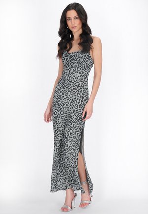 Kobieta o długich ciemnych włosach, ubrana w szarą, bezrękawnikową, długą sukienkę w panterkę z bocznym rozcięciem oraz srebrne sandały na wysokim obcasie.