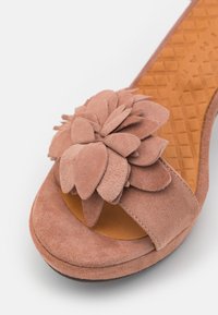 Sandale ouverte rose en suède pour femme, ornée de décorations florales superposées sur la lanière et dotée d'une semelle intérieure marron texturée.