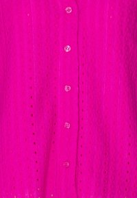 Heldere roze shirt van textuurstof met een subtiel patroon. Bevat zes ronde, roze knopen aan de voorkant.