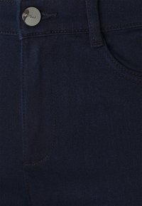 Tmavě modré džíny z denimu s přední kapsou a kovovým zapínáním. Látka má hladkou texturu a jemné detaily šití.