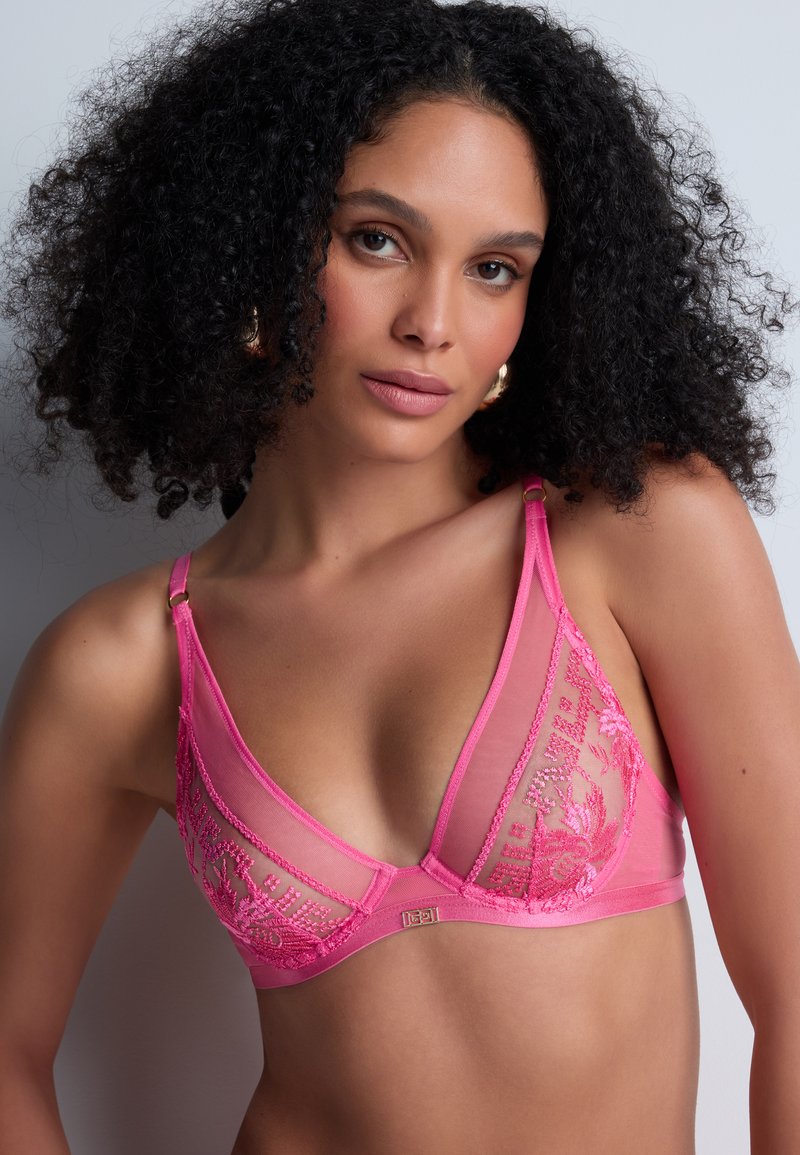 Bralette en dentelle rose avec des bonnets transparents, broderies florales et bretelles ajustables. Les accents en métal doré à la base rehaussent le design.