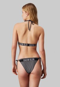 Bikini à rayures noires et blanches avec un col halter et des bas à nouer sur les côtés, présentant un logo "CALVIN KLEIN" bien visible sur les bandes.