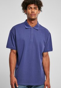 Polo shirt violet avec un col, des détails de boutons et des manches courtes. Fabriqué dans un tissu lisse et doux, légèrement ajusté.