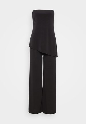 Musta, olkaimeton haalari, jossa on epäsymmetrinen helma. Valmistettu pehmeästä kankaasta, jossa on leveät suorat lahkeet. Yksinkertainen ja elegantti muotoilu.