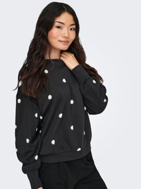 Black sweatshirt with white daisy embroidery, round neckline, long sleeves, ribbed cuffs, and hem, worn over black pants.