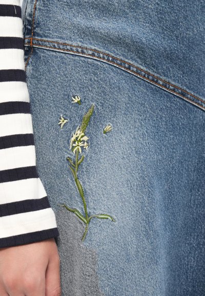 Jeanskjørt med grønn blomsterbroderi langs siden. Duken er lyseblå med strukturerte detaljer og oransje sømmer.