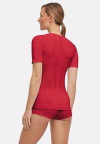 Maglietta atletica rossa attillata con maniche corte, design senza cuciture e pannello posteriore testurizzato. Abbinata a pantaloni corti a vita alta coordinati.