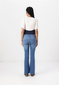 Blå flagrende jeans med høy midje og en marineblå midjebånd. Bak har de lommer og et lærmerke. Teksturert, ribbet hvit topp synlig.