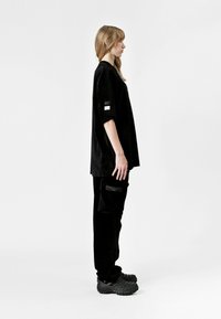 Camiseta oversized de pana negra con mangas cortas, combinada con pantalones de pana negra que tienen un bolsillo lateral. Calzado negro grueso.