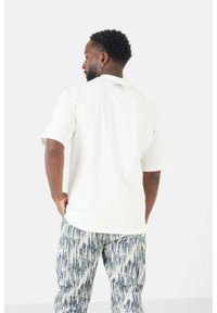 Witte T-shirt met korte mouwen en een standaard ronde hals, met een label aan de achterkant. Gecombineerd met blauw-witte patroonbroek.