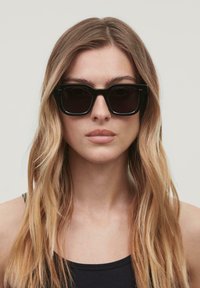 Mustad mustad sunglassid tumedate läätsedega. Valmistatud plastikust, paksu raamiga ja peene detailiga templis.