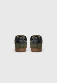 Pair of olive green suede sneakers with black collar and brown soles, viewed from the back, branded with FILA logo on heels.