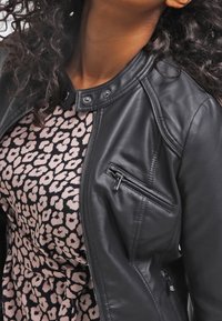 Black leather jacket with a snap collar, featuring side and chest zip pockets, layered over a patterned pink and black dress.