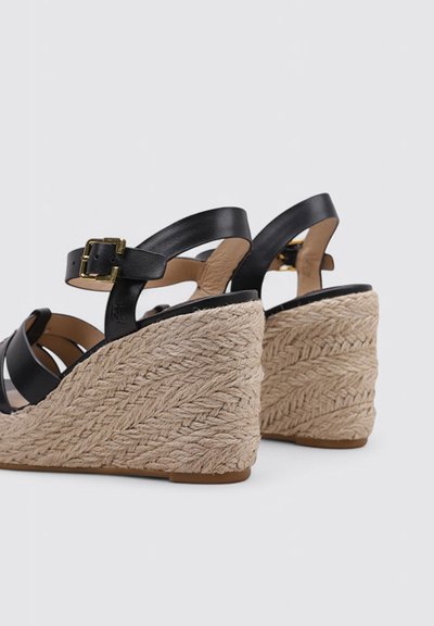 Sandalias cuña de cuero negro con tiras en el tobillo y hebillas doradas, con gruesos tacones de cuña de fibra natural trenzada.