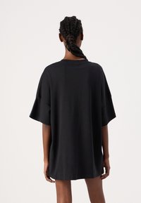 Tricou oversized negru, cu mâneci scurte și largi. Materialul pare neted. Are un guler clasic de tip crew și o croială lejeră. Fără modele sau accente.