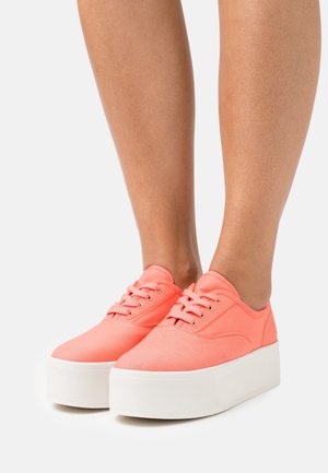 Sneakers di tela color corallo con punta arrotondata, suola piattaforma bianca e lacci coordinati. Texture liscia, dettagli di cucitura semplici.
