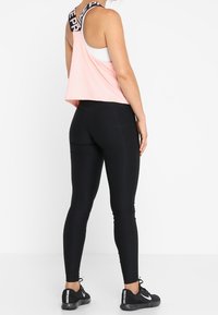 Top court rose avec des bretelles logo noires, associé à des leggings noirs ajustés. Les détails incluent des coutures contrastées et des chaussures de sport noires.