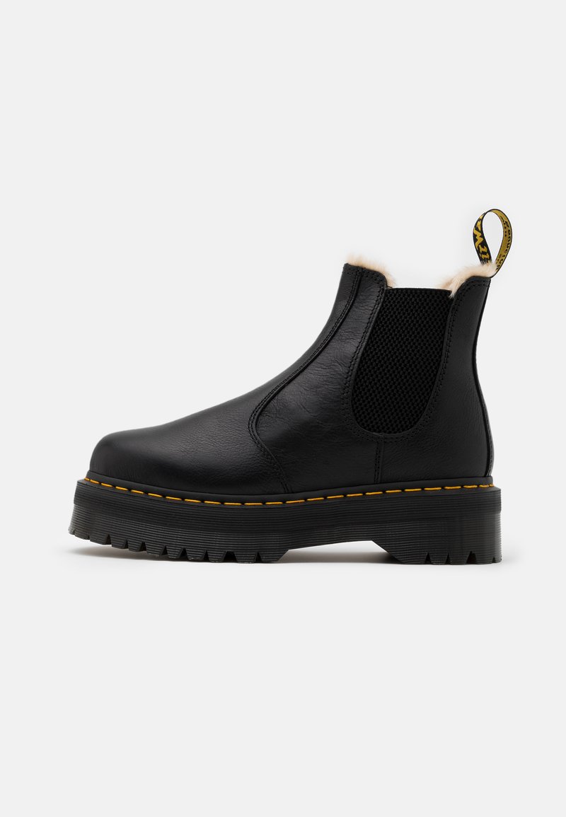 Bota de tornozelo em pele preta com painéis laterais elásticos, acabamento em pelúcia sintética, sola robusta e dentada, e detalhe em costura amarela. Apresenta um laço para puxar.