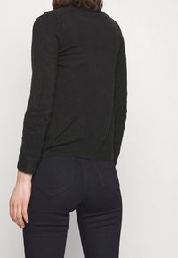 Czarny dziany sweter z długimi rękawami, dopasowany fason i prążkowany dół, w połączeniu z ciemnymi jeansami z klasycznym projektem kieszeni.