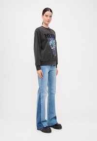 Svart crewneck sweatshirt med "Hero" grafikk og leoparddesign, parret med lyseblå flare jeans og chunky svarte plattformsko.