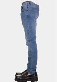 Jeans di denim blu a taglio slim con tasche posteriori, abbinati a mocassini neri con suola spessa. Tessuto semplice, senza motivi visibili.