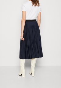 Marinblå plisserad midi-kjol med en elastisk linning, i kombination med knähöga vita klackstövlar. Slät textur, subtil fall och flödande silhuett.