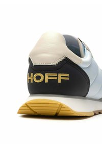 Zapatilla con un upper de cuero azul claro y negro, capucha blanca en el talón, logo dorado "HOFF" y suela de goma texturizada con parte inferior amarilla.