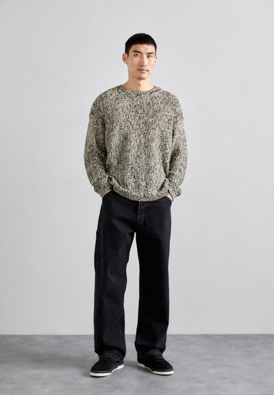 Knitted sweater in black and cream with a loose fit, paired with black wide-leg jeans and black sneakers. Smooth texture and casual design.