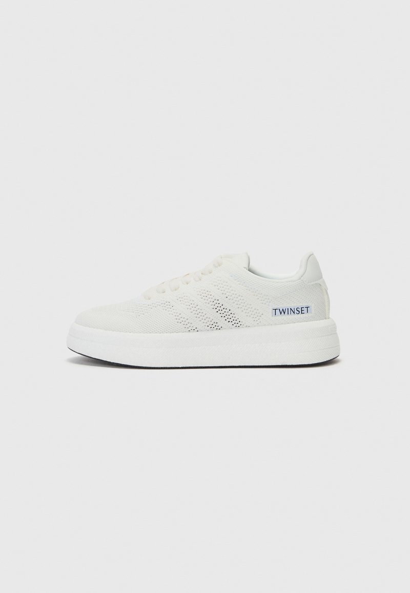 Hvit sneakers med mesh-overdel, teksturdetaljer, rund tå og kontrasterende marineblå logo. Har en tykk, hvit gummisåle.