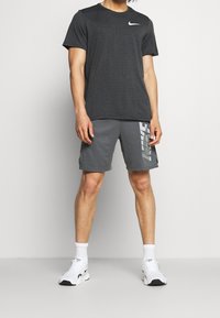 Dunkelgraues Nike-T-Shirt mit strukturiertem Muster, kombiniert mit grauen Shorts, die ein reflektierendes Logo aufweisen. Getragen mit weißen Sportschuhen und Socken.