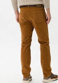 Bruna kordfläskbyxor med rak bendesign, utrustade med bakfickor och en texturerad tyg. Bärs med ett bälte och avslappnade skor.