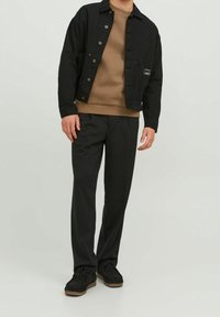 Chaqueta de mezclilla negra sobre un sudadera marrón, combinada con pantalones negros y zapatos negros. Presenta botones de metal y un detalle de bolsillo lateral.