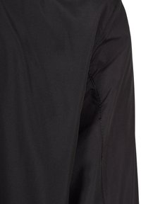 Gros plan sur un tissu noir montrant la couture et les points d'un vêtement, mettant en valeur la texture et les détails du matériau.